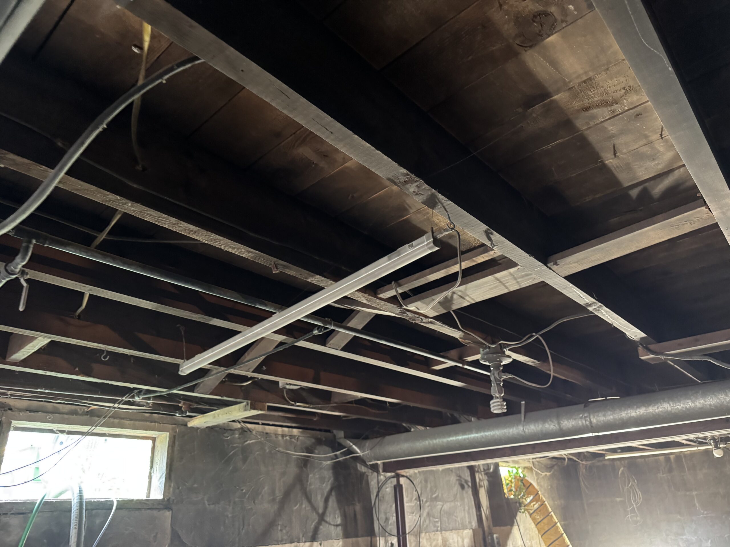 Fire Damage Sandblasting – Bristol, Vermont Before and after fire damage restoration in Bristol Vermont showing sandblasted wood floor joists and concrete basement walls