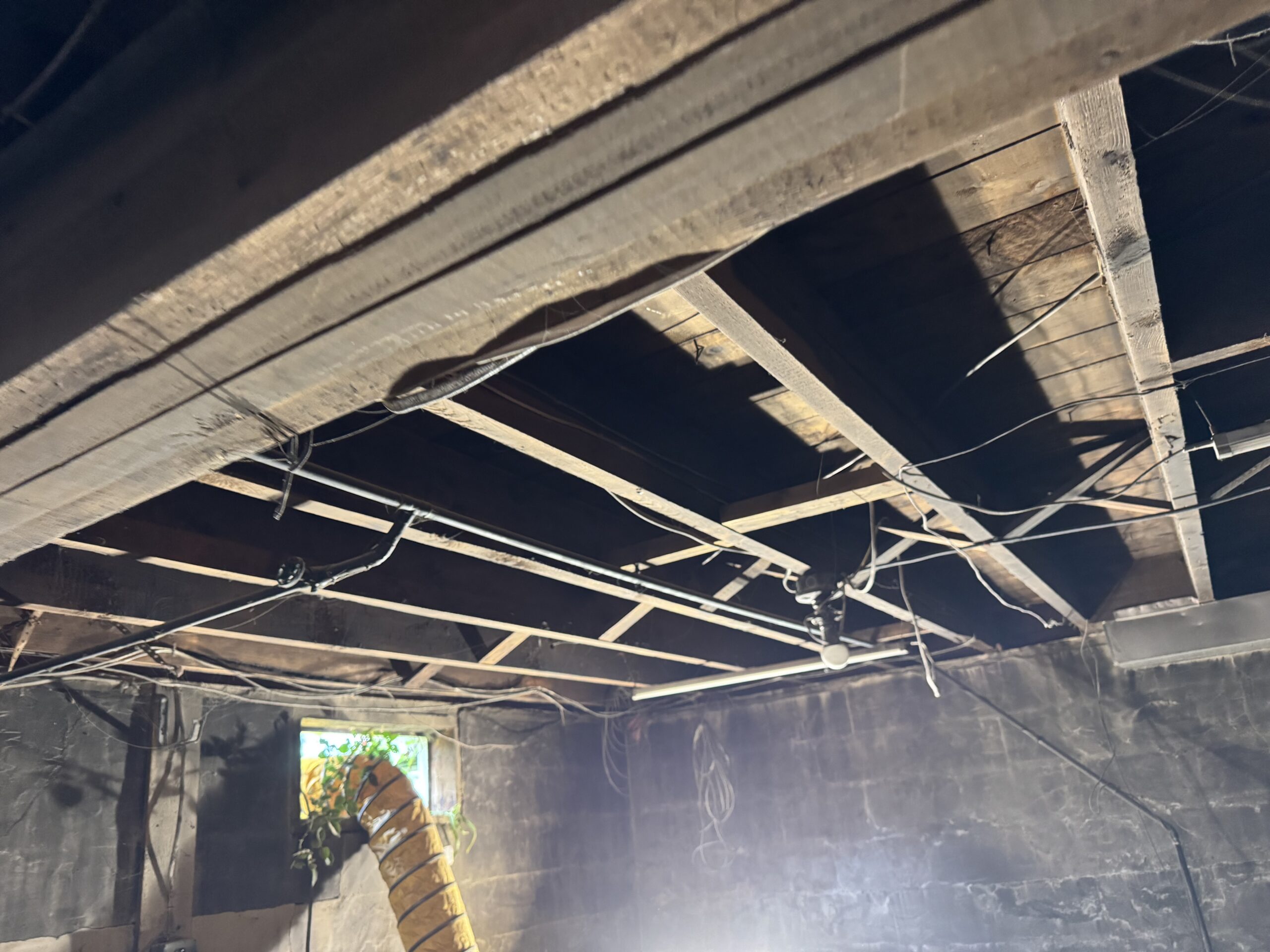 Fire Damage Sandblasting – Bristol, Vermont Before and after fire damage restoration in Bristol Vermont showing sandblasted wood floor joists and concrete basement walls